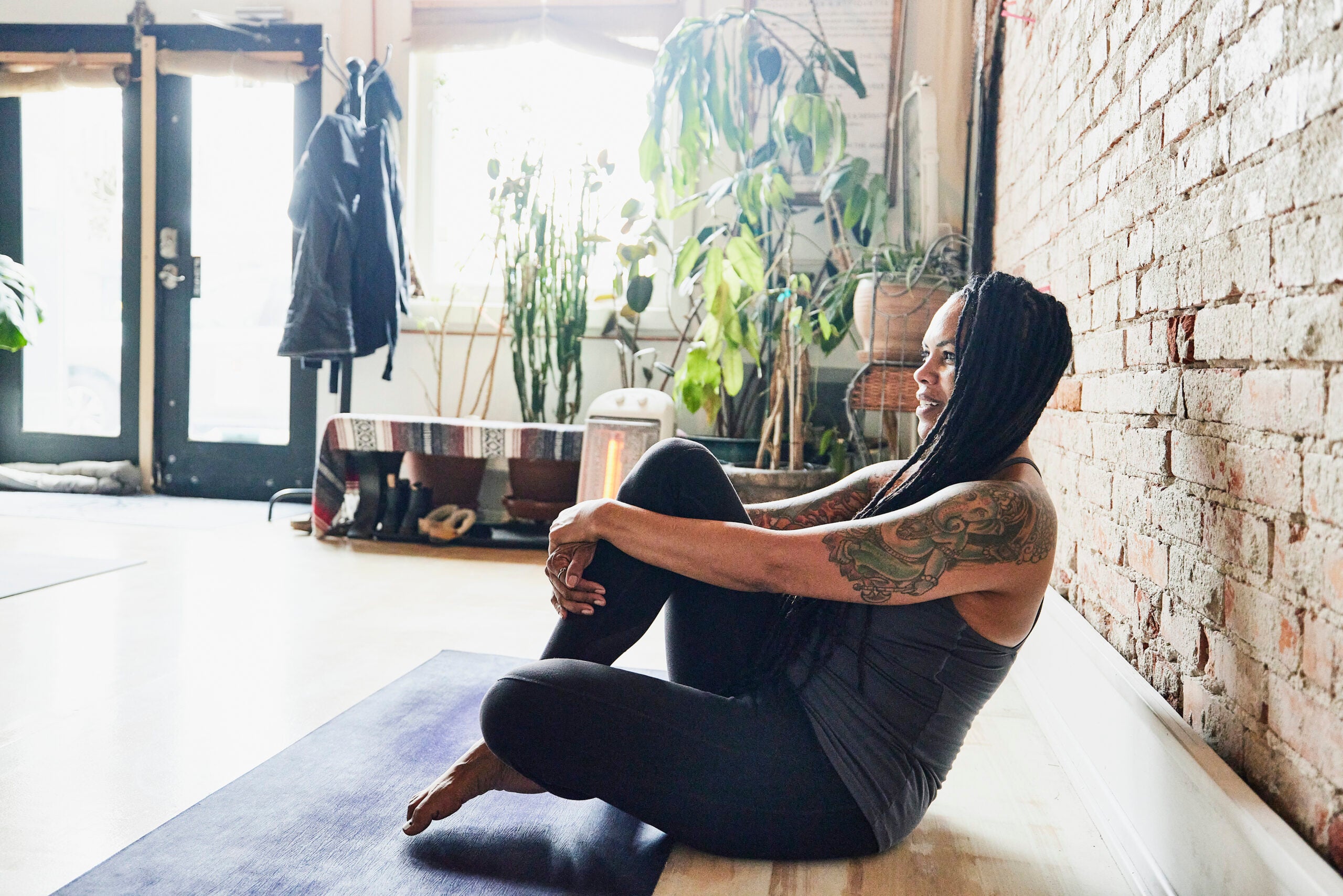 Yoga teacher sitting on her yoga mat at the front of class smiling and talking to students.